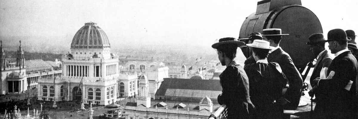 A wide-angle black and white historical photograph showing a group of people in late 19th-century attire, including hats and formal coats, looking out from a high vantage point. In the distance, the ornate, domed Administration Building of the 1893 World's Columbian Exposition is visible against a hazy horizon.